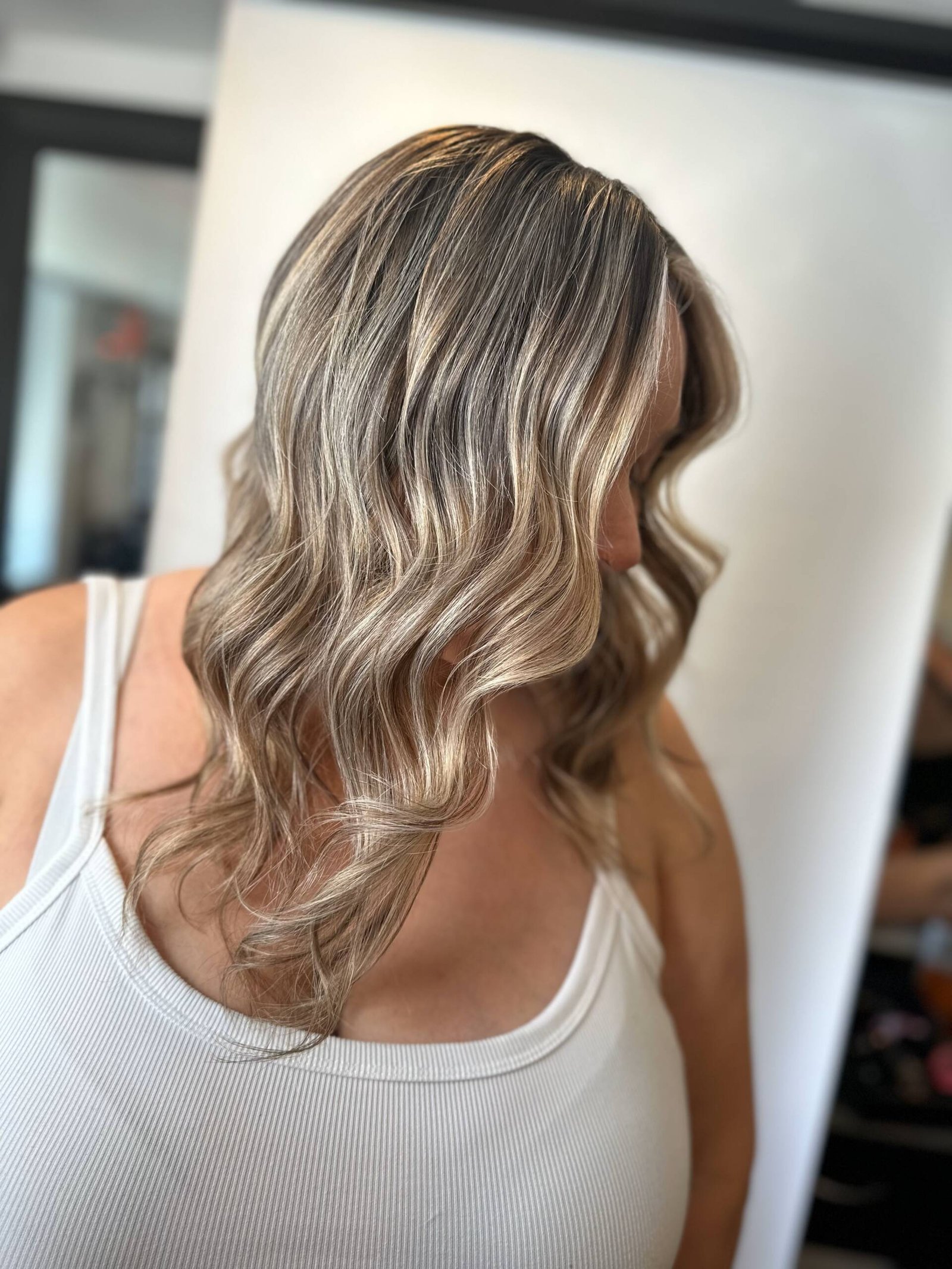 A woman with sun-kissed wavy hair showcasing Redken Shades EQ highlights and balayage.
